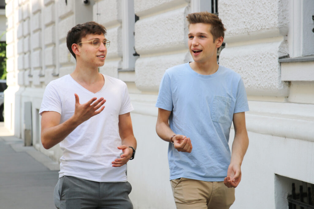 Zwei junge Männer gehen in einer Straße und unterhlaten sich. Kurze Sommerkleidung. Es sind die Gründer von Context Verify.